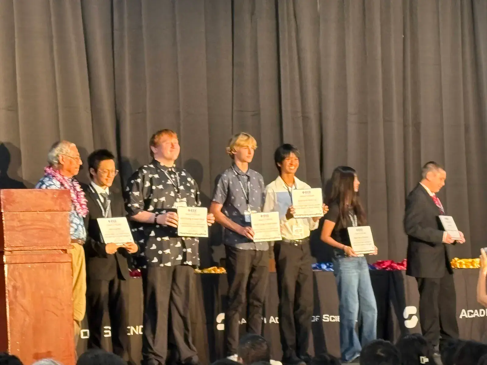 Students holding certificates on stage at an awards ceremony
