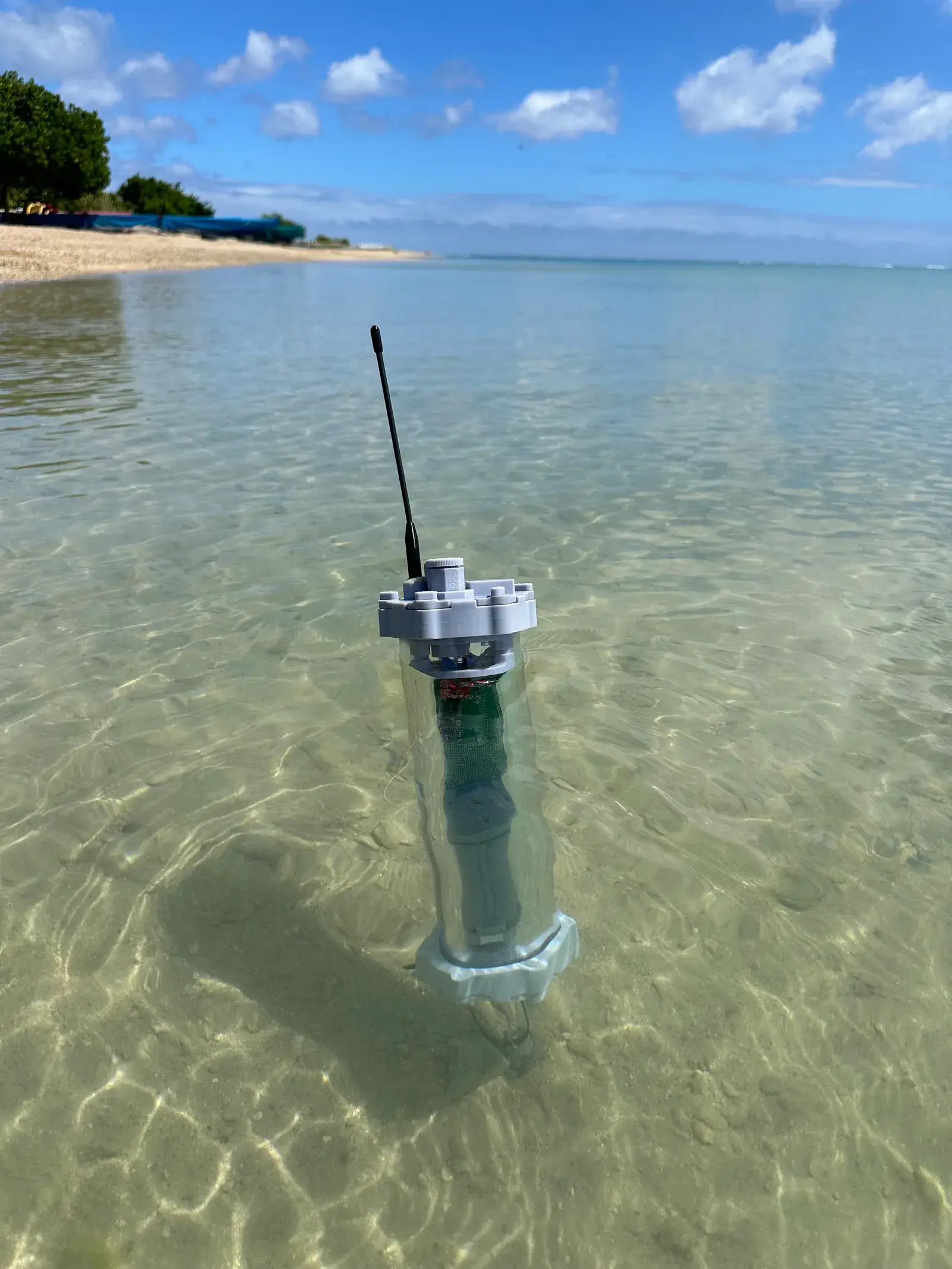 The MiSo sensor platform floating upright in clear shallow ocean water, antenna up