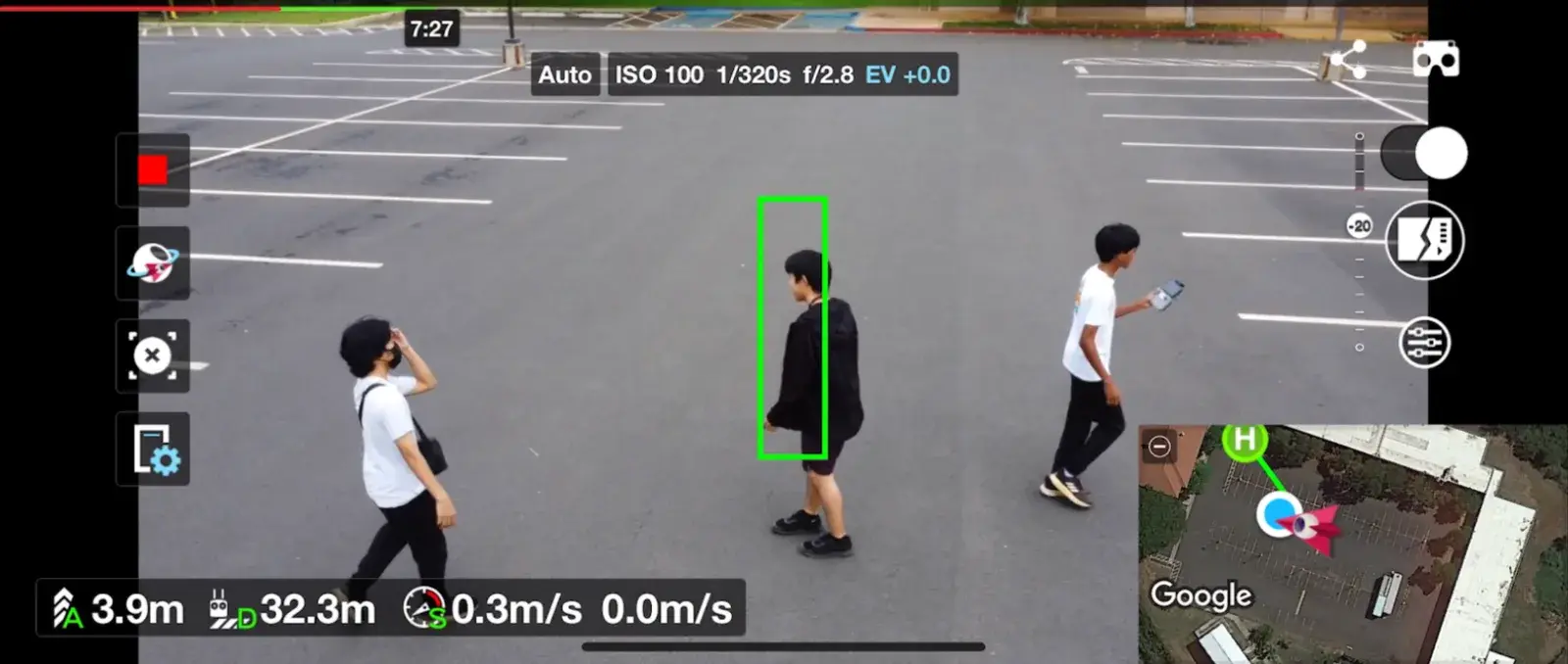 Drone view of a parking lot: a green tracking box locked on one person while two others walk past