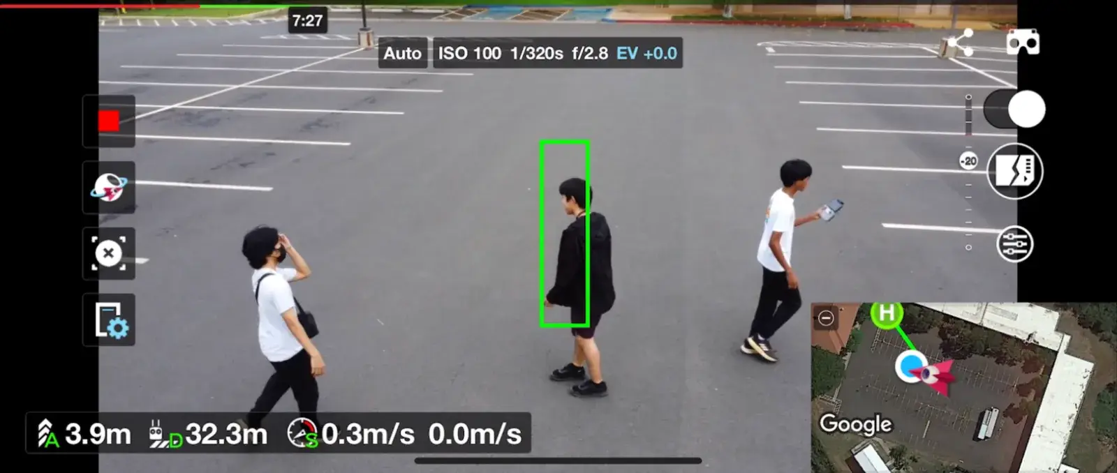 Drone view of a parking lot: a green tracking box locked on one person while two others walk past