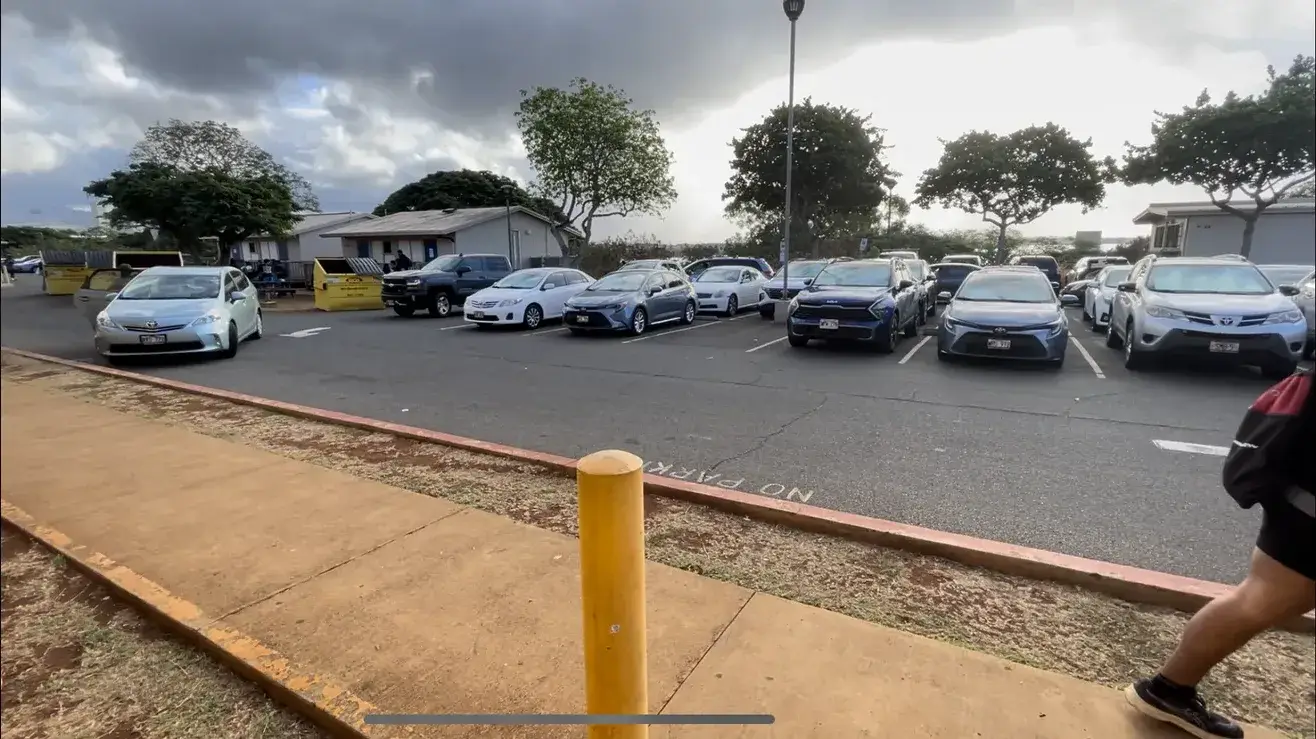 The filming site: a school parking lot with a line of parked cars and a traffic cone
